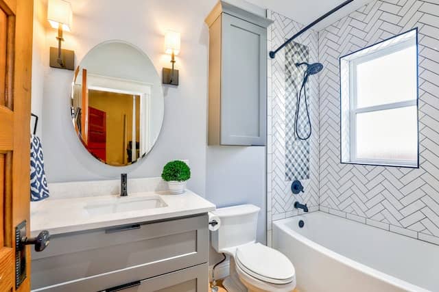 Remodeled bathroom with oval mirror, white tub, tiled walls and brown accents. Bathroom Remodeling company charlotte