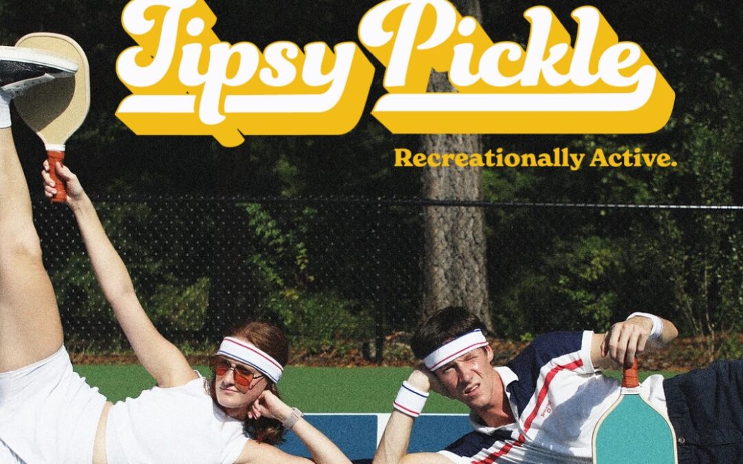Tipsy Pickel graphic with guy and girl sitting on pickle ball court.